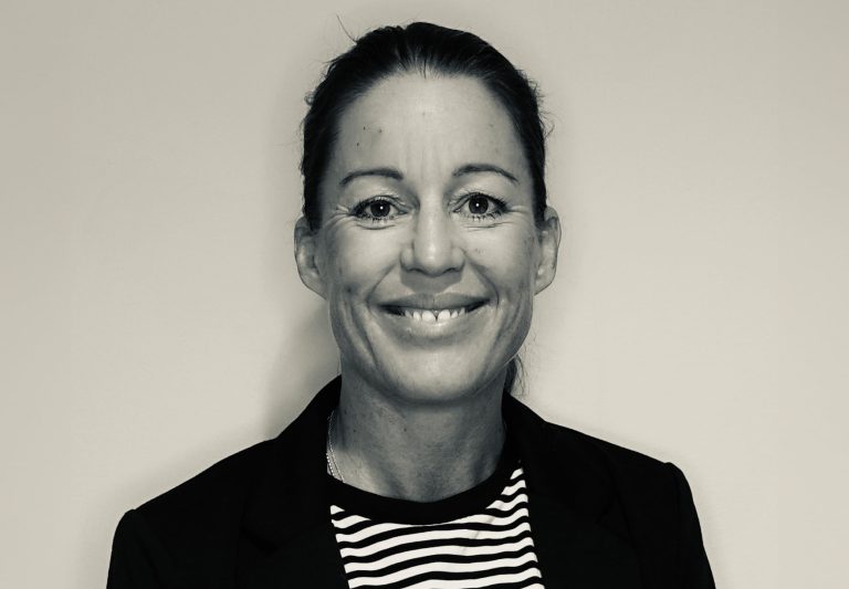 Jenny Eneroth porträtterad inomhus, leende mot kameran med neutral bakgrund