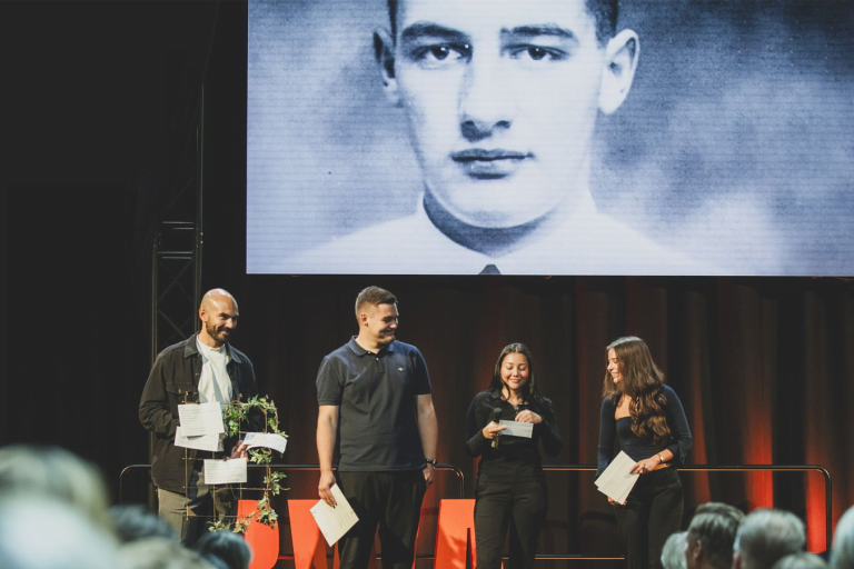 Eleverna Hugo Ericsson, Noor Mansourian och Felicia Mellbom står på en upplyst scen tillsammans med läraren Lukas Zayane. I förgrunden syns en publik som tittar på eleverna.