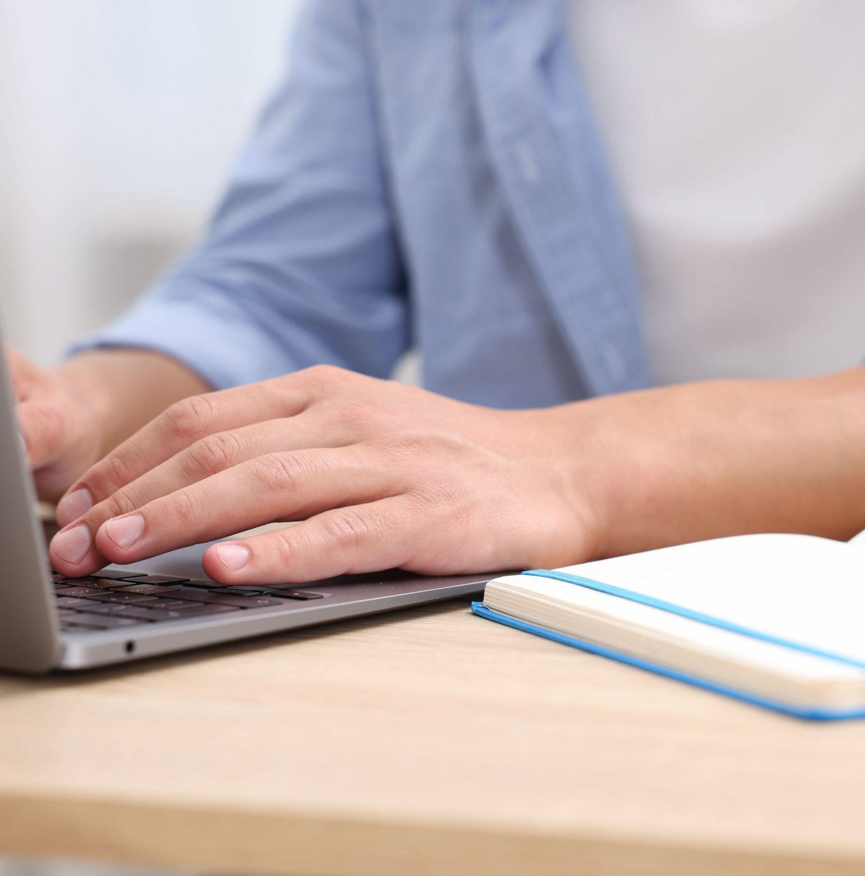 Person som arbetar vid laptop med anteckningsbok bredvid.