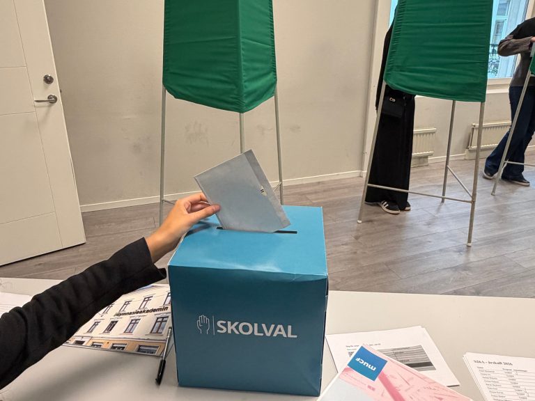 Foto på en hand som stoppar en valsedel i urnan.