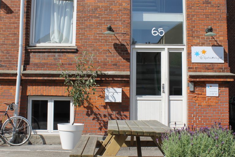 Fotot visar fasaden på en skola med fönster, dörr och blommor utanför.